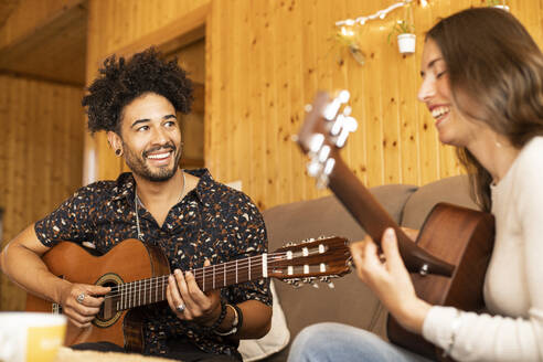 Lächelndes Paar spielt Gitarre, während es zu Hause sitzt - LJF01882