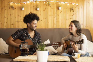 Paar lächelnd beim Üben mit Gitarre zu Hause sitzend - LJF01884