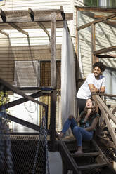 Man smiling while standing by woman sitting on staircase - LJF01894