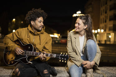 Freundin hört ihrem Freund zu, der singt und Gitarre spielt, während er auf einer Mauer sitzt - LJF01922