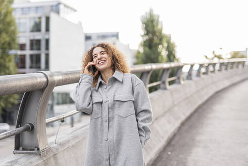 Fröhliche junge Afro-Frau, die auf einer Brücke in der Stadt steht und mit ihrem Handy spricht - MEF00041