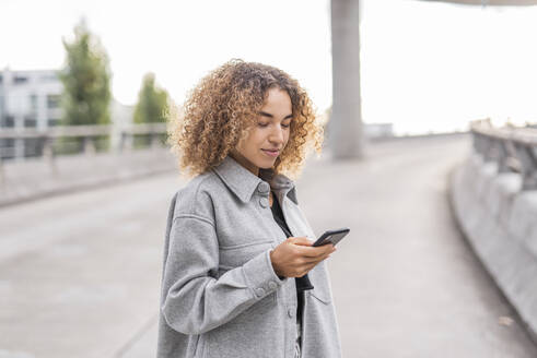 Schöne junge Afro-Frau, die ein Smartphone benutzt, während sie auf einer Brücke in der Stadt steht - MEF00043