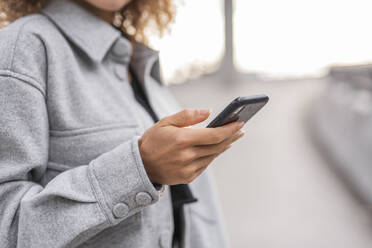 Junge Frau, die ihr Smartphone benutzt, während sie auf einer Brücke in der Stadt steht - MEF00044