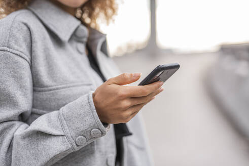 Junge Frau, die ihr Smartphone benutzt, während sie auf einer Brücke in der Stadt steht - MEF00044