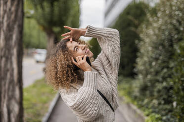 Blonde Afro-Frau schaut auf, während sie mit einem Handy spricht - MEF00047