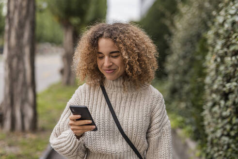 Lächelnde junge Frau, die mit ihrem Smartphone in der Stadt Textnachrichten verschickt - MEF00048