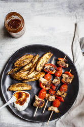 Gyros-Hähnchenspieße mit Tomaten, Paprika, Kartoffelspalten im Teller mit Tzatziki auf dem Tisch - SBDF04452