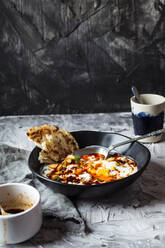 Frühstück mit Joghurt und würziger Paprikabutter auf pochierten Eiern in einer Schale neben einer Kaffeetasse auf dem Tisch - SBDF04469