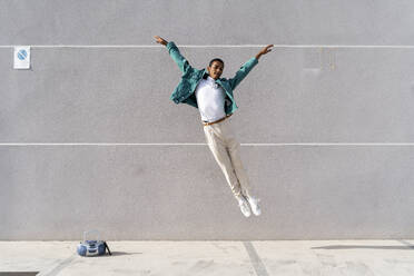 Junger Mann mit Radio auf dem Fußweg, der gegen eine graue Wand springt - AFVF07797