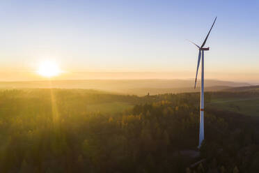 Die untergehende Sonne beleuchtet eine im Herbstwald stehende Windkraftanlage - WDF06433