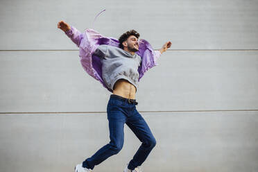 Cheerful man jumping against gray wall - MIMFF00318