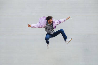 Junger Mann springt fröhlich gegen die Wand - MIMFF00321