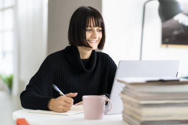 Lächelnde junge Studentin mit Laptop beim Schreiben im Studienraum - GIOF09927