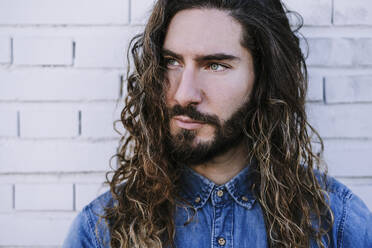 Thoughtful young man with long hair against brick wall - EBBF01727