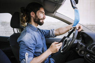 Handsome man with mobile phone sitting in car during COVID-19 - EBBF01759