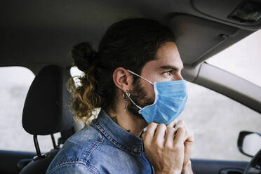 Stilvoller junger Mann, der im Auto eine Gesichtsschutzmaske anpasst - EBBF01762