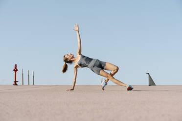 Sportlerin beim Yoga mit erhobener Hand, die auf einer Seite balanciert - RDGF00275