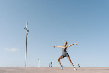 Sportswoman with arms outstretched exercising against sky - RDGF00281