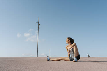 Smiling sportswoman sitting on ground, relaxing on a sunny day - RDGF00285