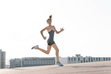 Glückliche Sportlerin beim Laufen gegen den klaren Himmel in der Stadt - RDGF00291