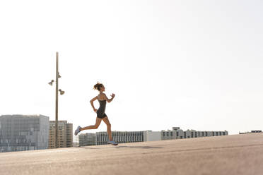 Weibliche Sportlerin beim Joggen an einem sonnigen Tag in der Stadt - RDGF00292