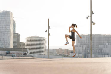 Mittlere erwachsene Sportlerin bei einer Sprungübung an einem sonnigen Tag in der Stadt - RDGF00293