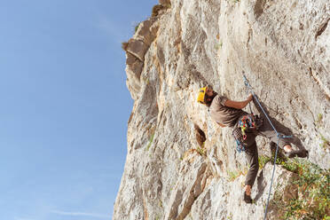 Sportive male alpinist climbing on sheer cliff in summer day - ADSF18803