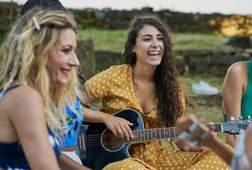 Lächelnde Frau spielt Gitarre und hat Spaß mit einer Gruppe von Freunden - CAVF91390