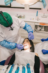 Unrecognizable orthodontist in sterile gloves putting transparent braces on teeth of woman in clinic - ADSF18831