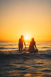 Silhouetten von fitten Frauen auf Paddle Board im Meerwasser auf dem Hintergrund des Sonnenuntergangs Himmel im Sommer - ADSF18837