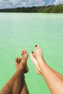 Heterosexual couple legs over ocean on sunny day - JMPF00705