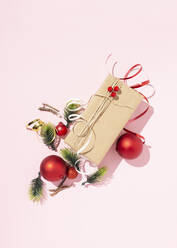 Draufsicht auf ein in Bastelpapier eingewickeltes und mit Schnur verschnürtes Geschenk, angeordnet auf einem rosa Hintergrund mit Weihnachtskugeln und verschiedenen Dekorationen - ADSF18907