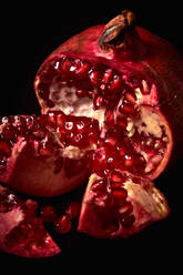 Close up of fresh ripe halved pomegranate and seeds on black background - ADSF18942