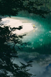 From above of anonymous traveler admiring view of tranquil lake with bright water surrounded by green forest in Italy - ADSF18969