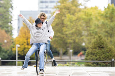 Carefree woman sitting with male friend on bicycle in park - GGGF00459