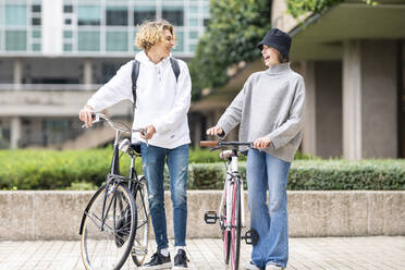 Cheerful friends standing with bicycle on footpath - GGGF00467