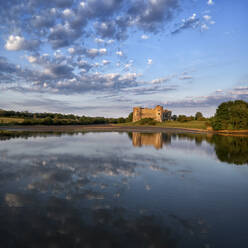 UK, Wales, Pembrokeshire, Wolken, die sich auf der glänzenden Oberfläche des Carew River in der Abenddämmerung spiegeln, mit Carew Castle im Hintergrund - ALRF01766