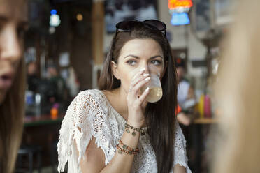 Young woman drinking by female friends at restaurant - AJOF00957