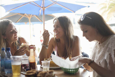 Glückliche Freundinnen beim Mittagessen in einem Strandrestaurant im Urlaub - AJOF00958