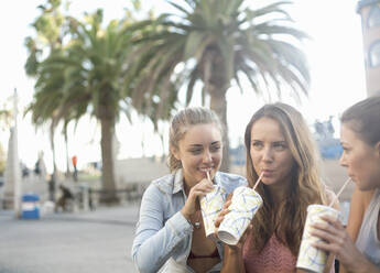 Female friends drinking chilled drinks at beach during vacation - AJOF00964