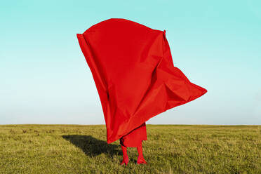 Frau bedeckt sich mit rotem Stoff und steht auf einem Feld vor blauem Himmel - ERRF04856