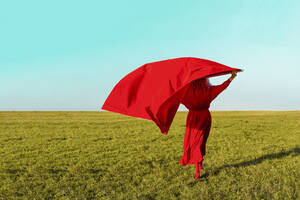 Senior woman with red fabric while standing on grass during sunny day - ERRF04860