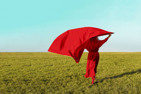 Ältere Frau mit rotem Stoff im Gras stehend an einem sonnigen Tag - ERRF04860