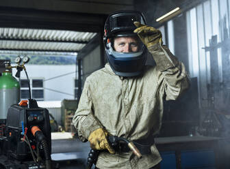 Handwerker mit Schweißerschutzhelm, der eine Schweißmaschine hält, während er in einer Fabrik steht - CVF01628