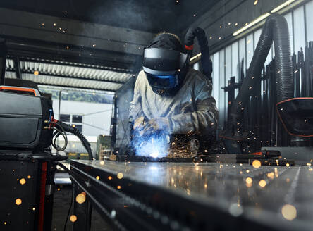 Metal worker wearing protective workwear welding metal while working at factory - CVF01630