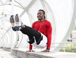 Smiling athlete doing handstand on bench at walkway - JCCMF00142