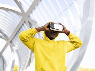 Sportsman using virtual reality headset while standing at elevated walkway - JCCMF00146