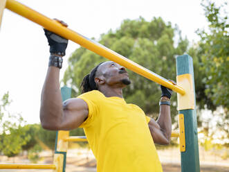 Male athlete doing chin-ups while exercising on road at park - JCCMF00157