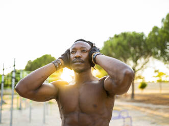 Sportsman wearing headphones listening music while standing at park - JCCMF00162