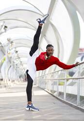 Sportsman stretching while doing splits standing on walkway - JCCMF00184